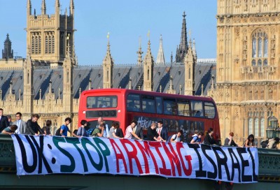 Protesters hanging a banner saying "Stop Arming Israel" from Westminster Bridge with the Palace of Westminster in the background
