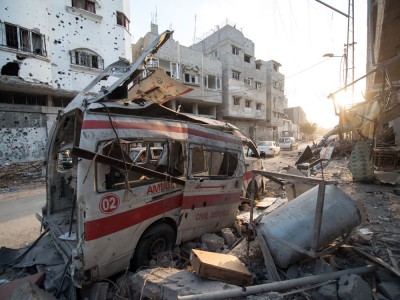 A wrecked ambulance surrounded by debris and damaged buildings