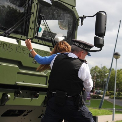A policeman drags a woman away from a military truck with graffiti on it